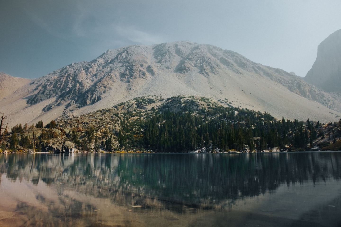 A mountain and pine forest reflect in a still lake.