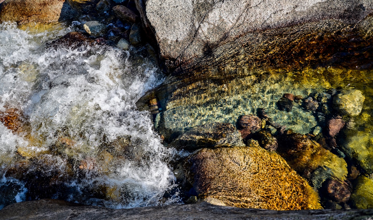 Clear river water flows over smooth rocks.