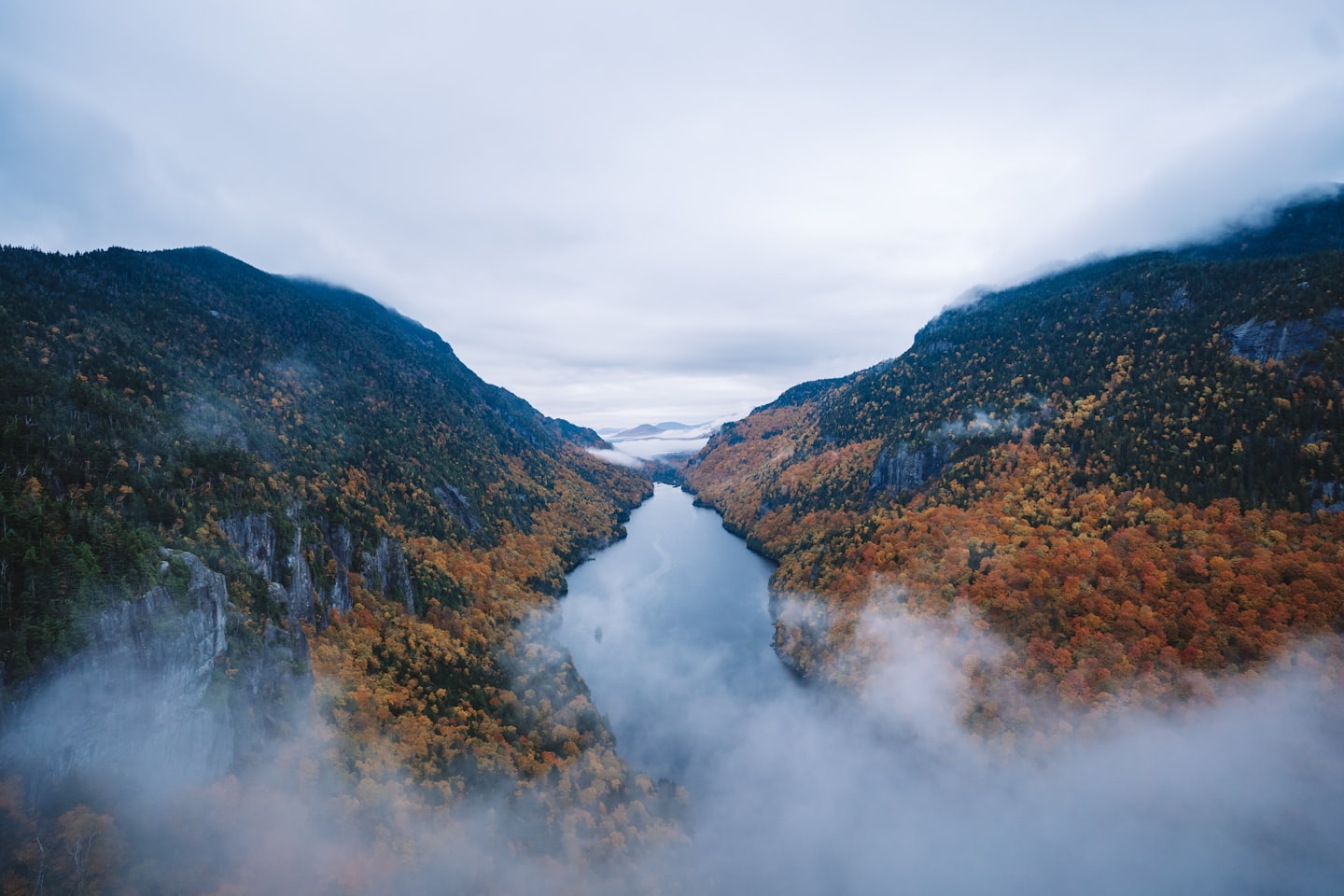 Winding river between autumn mountainsides with mist.