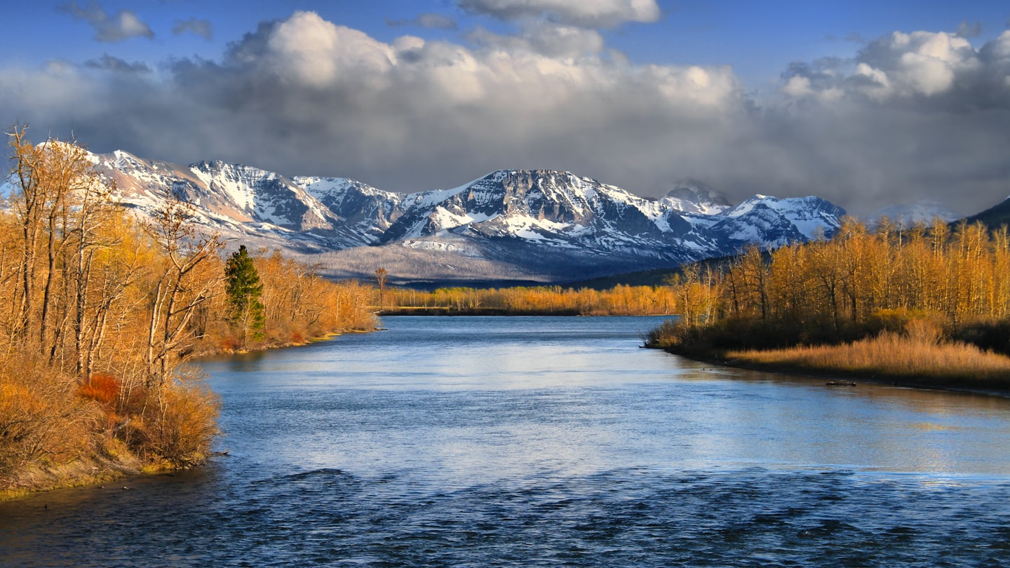 A river flows through a valley with golden autumn trees.