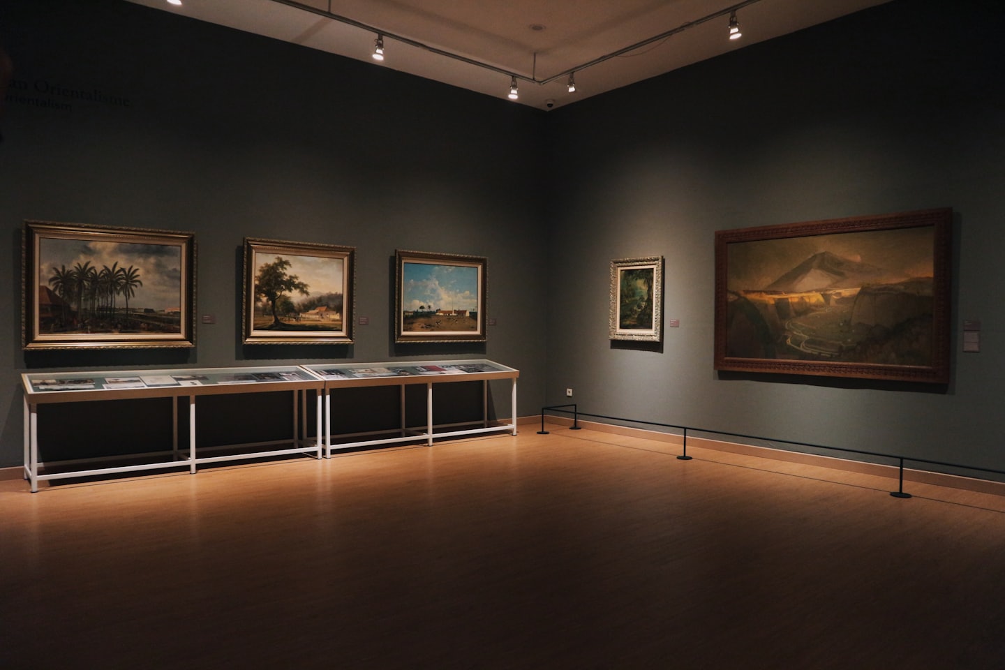 Empty art gallery with landscape paintings on grey walls.